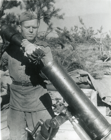 Советский артиллерист заряжает 120-мм полковой миномет образца 1938 г. одной из минометных частей 7-й гвардейской армии