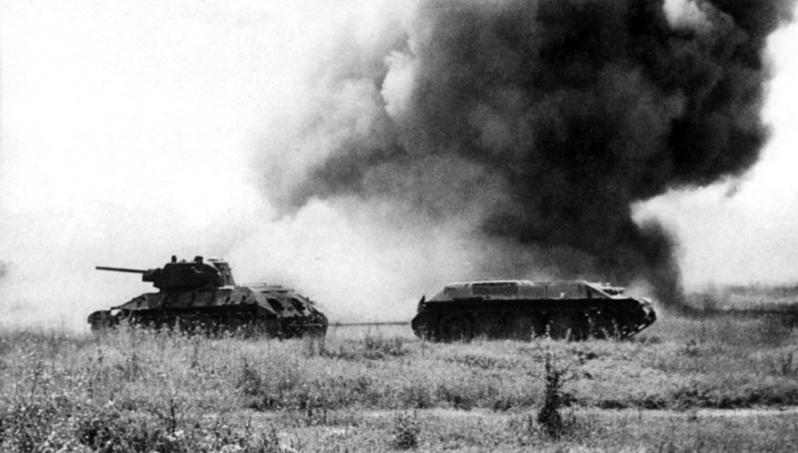 Буксировка подбитого танка Т-34 с поля боя тягачом на базе Т-34 (без башни) под обстрелом противника. Лето 1943