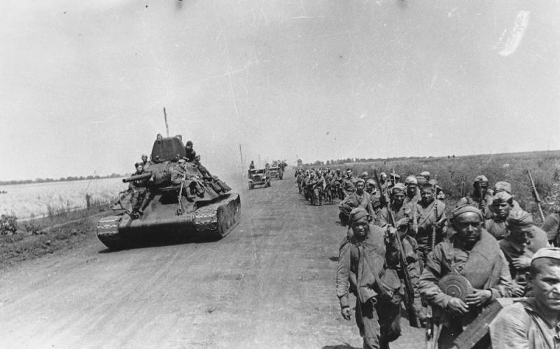 Танк Т-34 и колонна советских солдат на марше по дороге под Белгородом. Курская дуга. Август 1943